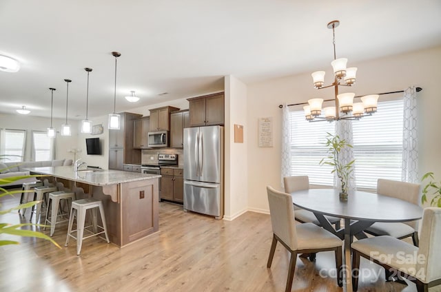 kitchen featuring light stone countertops, appliances with stainless steel finishes, light wood-type flooring, a chandelier, and pendant lighting