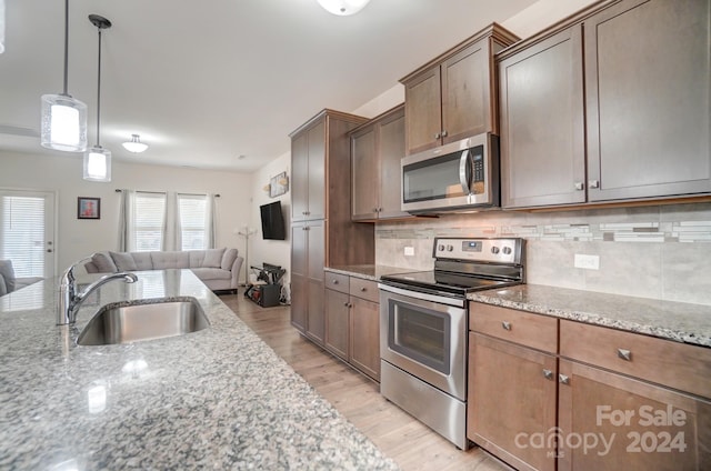 kitchen featuring sink, light stone counters, backsplash, light hardwood / wood-style floors, and stainless steel appliances