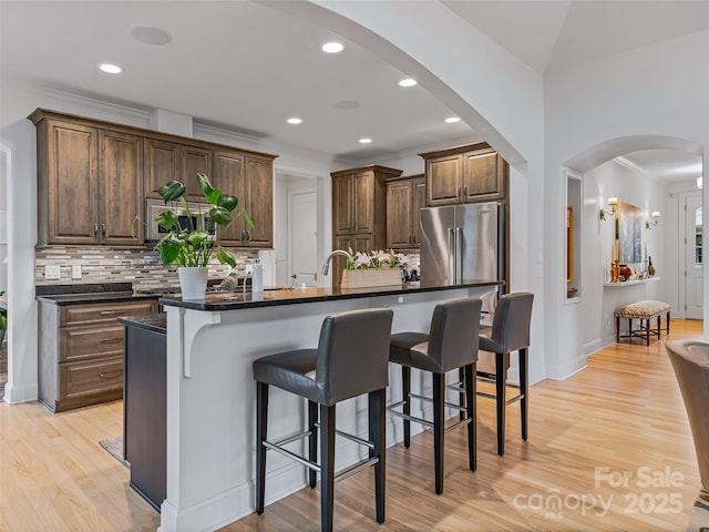 kitchen with a center island with sink, decorative backsplash, a kitchen bar, high quality fridge, and light hardwood / wood-style flooring