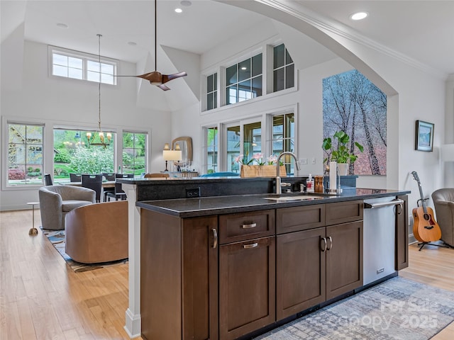 kitchen with a center island with sink, stainless steel dishwasher, sink, light hardwood / wood-style flooring, and dark brown cabinetry