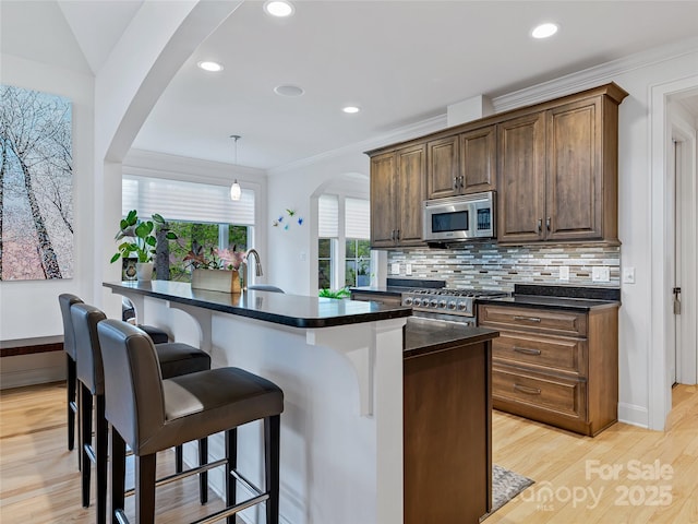 kitchen featuring a center island with sink, backsplash, decorative light fixtures, range, and light hardwood / wood-style flooring