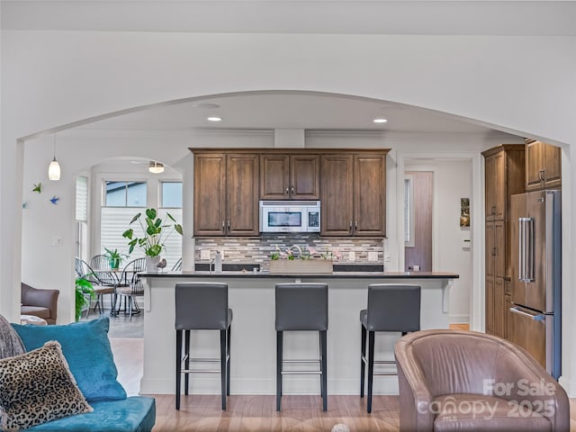 kitchen with a breakfast bar area, decorative backsplash, light wood-type flooring, and stainless steel appliances