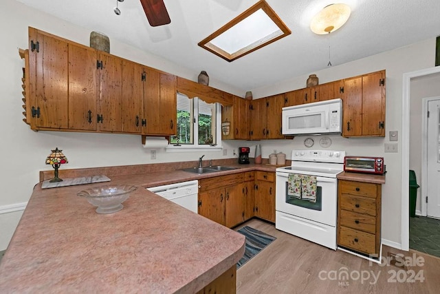 kitchen with light hardwood / wood-style floors, kitchen peninsula, sink, white appliances, and a skylight