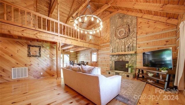 living room featuring wooden walls, light hardwood / wood-style flooring, wooden ceiling, a notable chandelier, and a stone fireplace