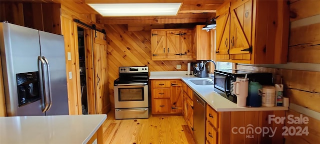 kitchen featuring wood walls, stainless steel appliances, light hardwood / wood-style flooring, and sink