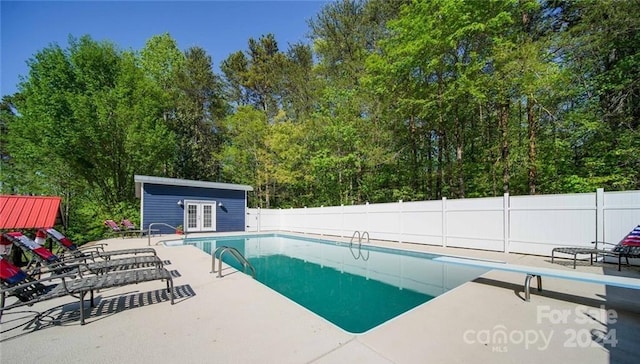 view of swimming pool featuring an outdoor structure, a diving board, and a patio