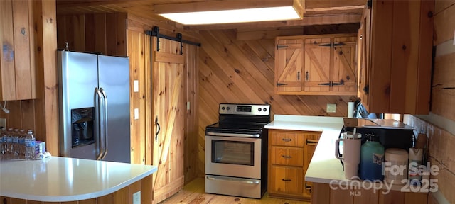 kitchen featuring wooden walls, stainless steel appliances, a barn door, and kitchen peninsula