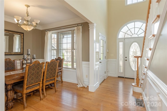 entrance foyer with a chandelier, crown molding, light wood-type flooring, and decorative columns