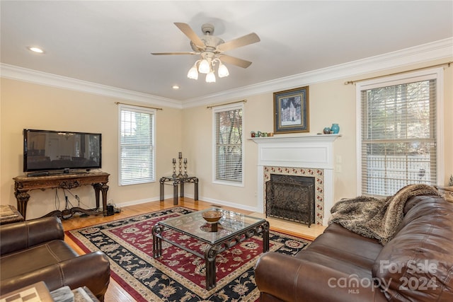 living room with a tiled fireplace, ceiling fan, light wood-type flooring, and ornamental molding