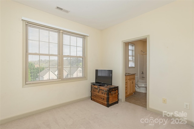 bedroom featuring visible vents, baseboards, light colored carpet, and ensuite bathroom