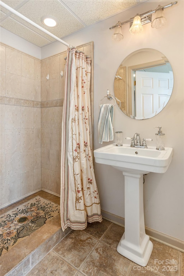 full bath featuring a tile shower, a paneled ceiling, baseboards, and a sink