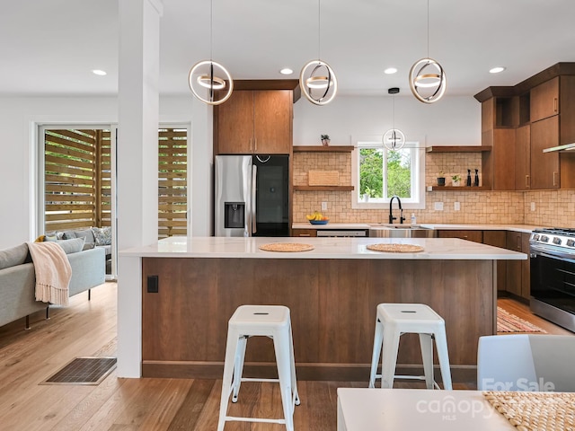 kitchen featuring sink, backsplash, stainless steel appliances, light hardwood / wood-style flooring, and pendant lighting