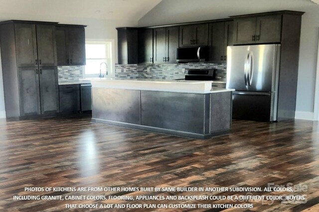 kitchen with dark hardwood / wood-style floors, decorative backsplash, appliances with stainless steel finishes, and vaulted ceiling