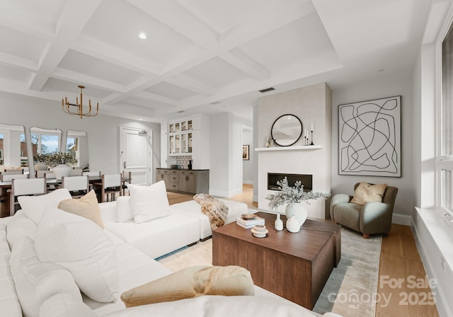 living room with a fireplace, beamed ceiling, light hardwood / wood-style flooring, coffered ceiling, and a notable chandelier