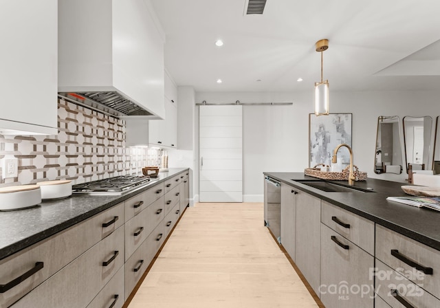 kitchen with a barn door, stainless steel appliances, premium range hood, sink, and decorative light fixtures