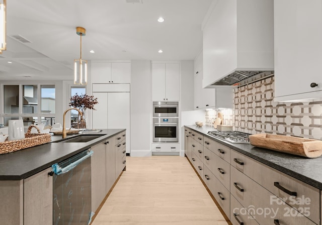 kitchen with white cabinets, appliances with stainless steel finishes, hanging light fixtures, custom range hood, and sink