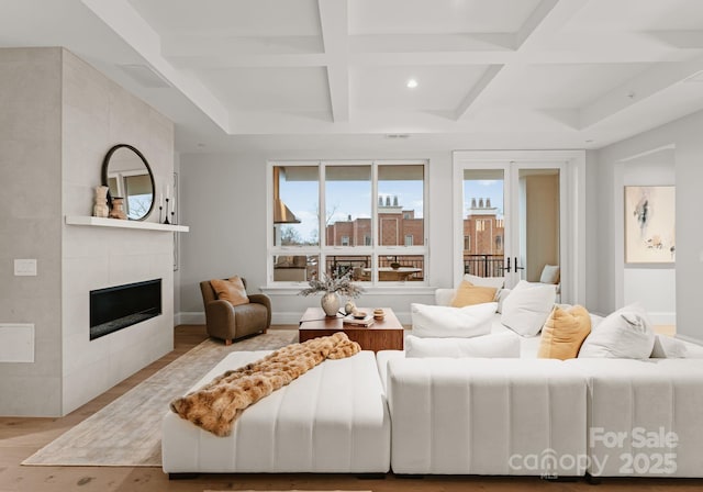 living room featuring coffered ceiling, a tile fireplace, light wood-type flooring, and beamed ceiling