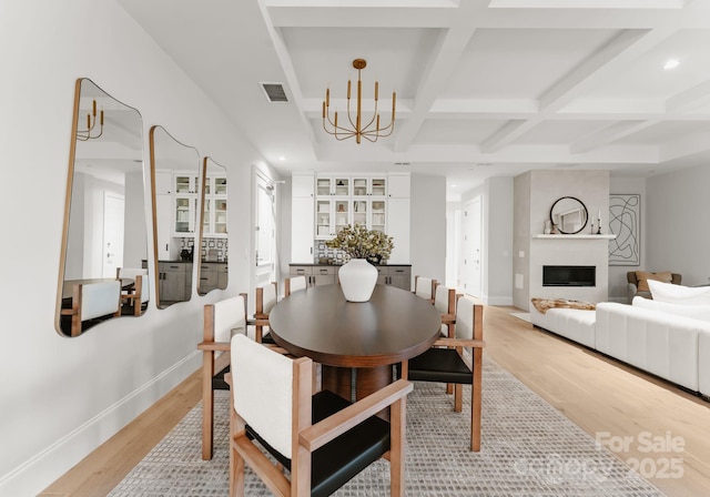 dining area featuring coffered ceiling, a chandelier, light wood-type flooring, a fireplace, and beam ceiling