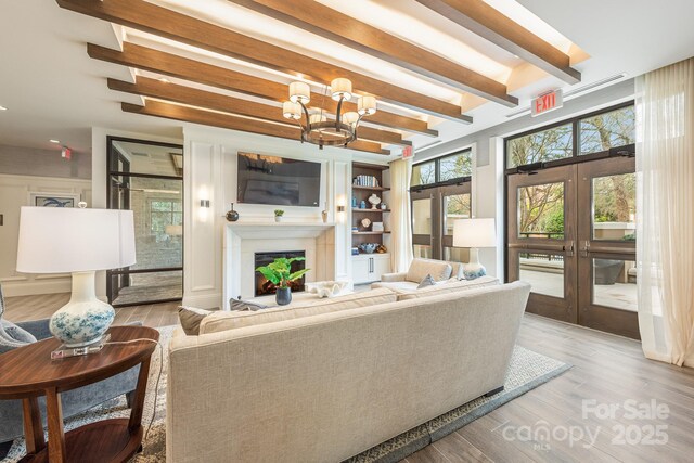 living room with beam ceiling, french doors, an inviting chandelier, and wood-type flooring