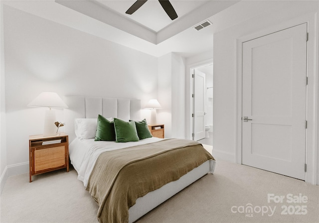 carpeted bedroom featuring ensuite bathroom, ceiling fan, and a tray ceiling