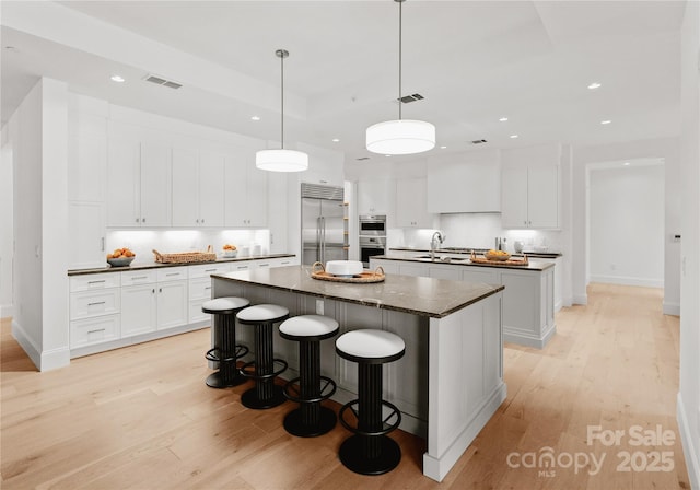 kitchen with appliances with stainless steel finishes, pendant lighting, white cabinets, a center island, and light hardwood / wood-style floors