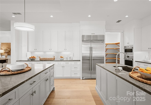 kitchen with sink, hanging light fixtures, stainless steel appliances, dark stone counters, and white cabinets