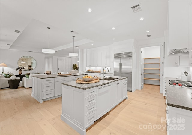 kitchen featuring white cabinets, sink, hanging light fixtures, an island with sink, and stainless steel built in refrigerator