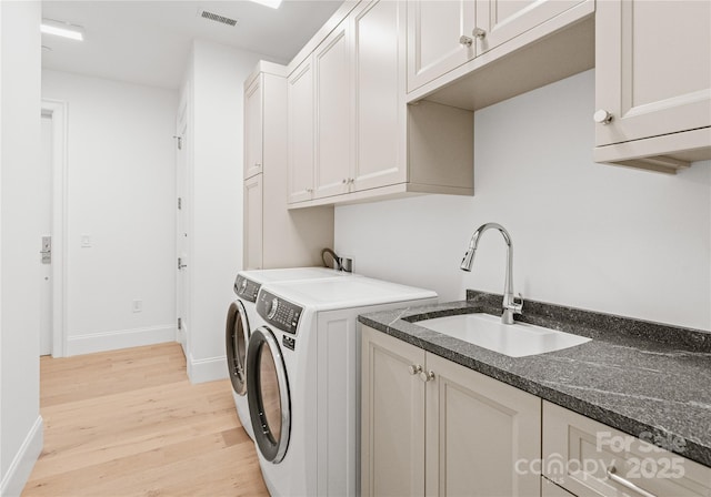 clothes washing area with cabinets, sink, washer and dryer, and light hardwood / wood-style floors