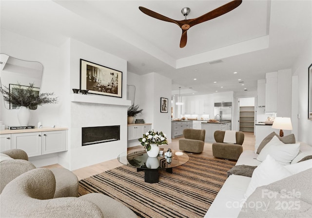 living room with ceiling fan, sink, and a tray ceiling