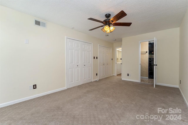 unfurnished bedroom with light carpet, a textured ceiling, two closets, and ceiling fan