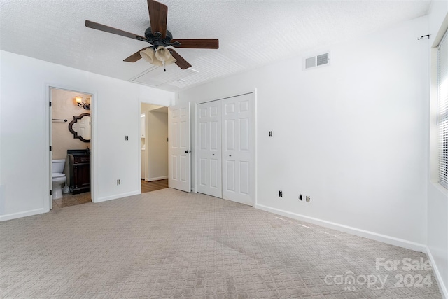 unfurnished bedroom with ensuite bathroom, ceiling fan, a textured ceiling, light colored carpet, and a closet