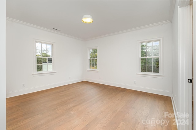 empty room with a wealth of natural light, crown molding, and light wood-type flooring