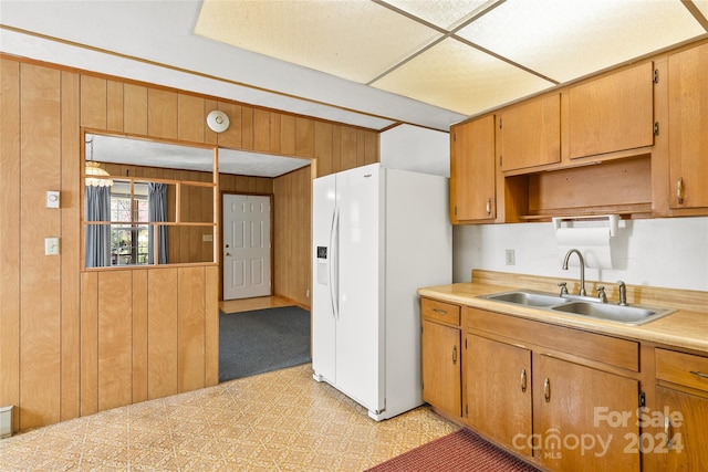 kitchen with wooden walls, white fridge with ice dispenser, sink, and light colored carpet