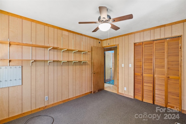 unfurnished bedroom featuring wood walls, ceiling fan, carpet flooring, and a closet