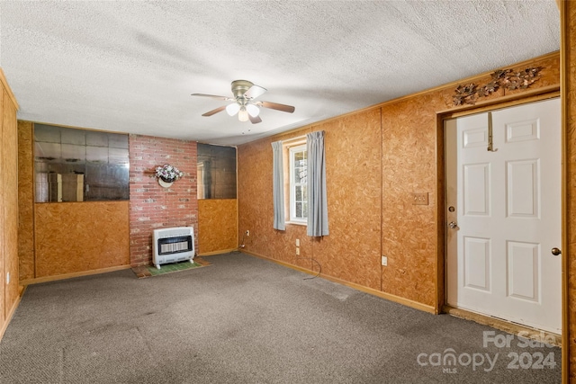 carpeted empty room with brick wall, a textured ceiling, ceiling fan, and a wood stove