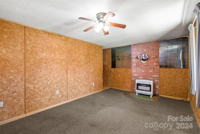 carpeted spare room with ceiling fan, a wood stove, brick wall, and a textured ceiling