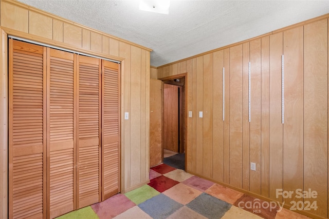 unfurnished bedroom with wood walls, a closet, and a textured ceiling