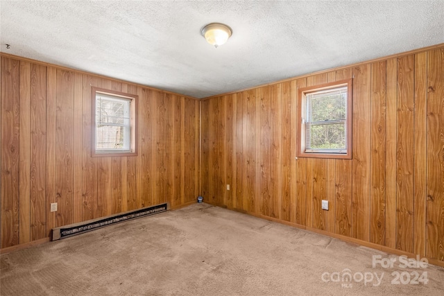 carpeted spare room featuring wood walls, a textured ceiling, and a baseboard radiator