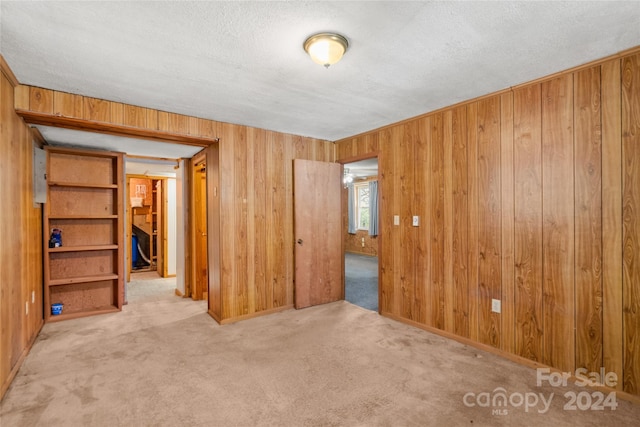 carpeted spare room featuring a textured ceiling and wood walls