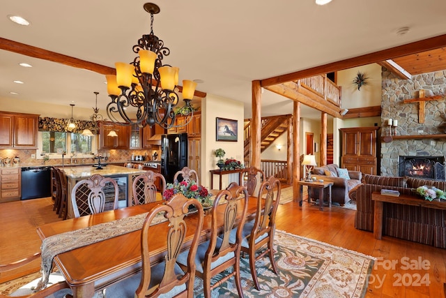 dining room featuring light hardwood / wood-style flooring, a chandelier, beamed ceiling, and a stone fireplace