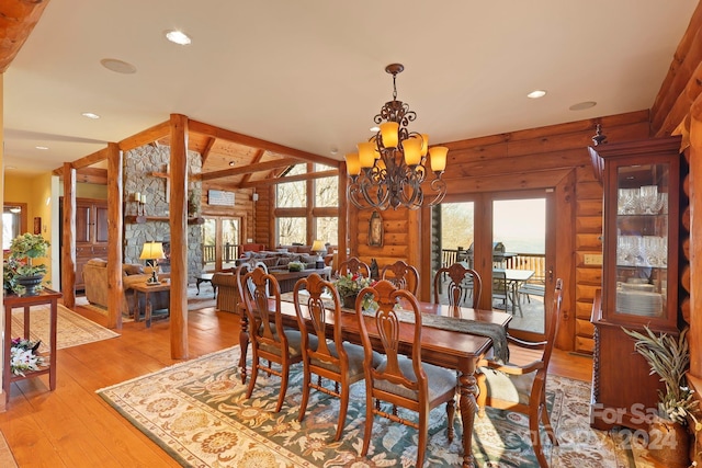 dining space with rustic walls, vaulted ceiling with beams, a chandelier, and light wood-type flooring