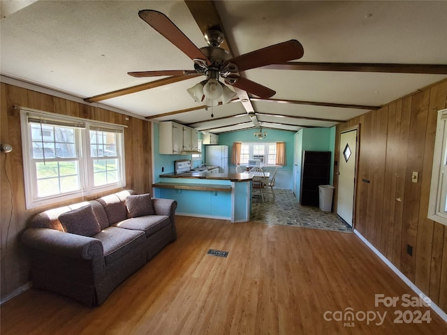 unfurnished living room with wooden walls, vaulted ceiling with beams, ceiling fan, and hardwood / wood-style flooring