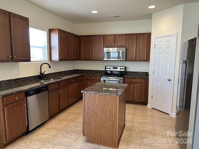 kitchen with appliances with stainless steel finishes, a kitchen island, dark stone countertops, light tile floors, and sink