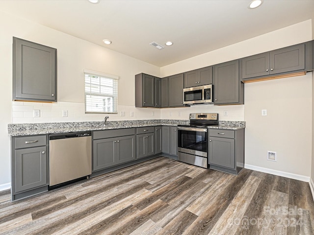 kitchen with gray cabinets, light stone counters, stainless steel appliances, and dark wood-type flooring