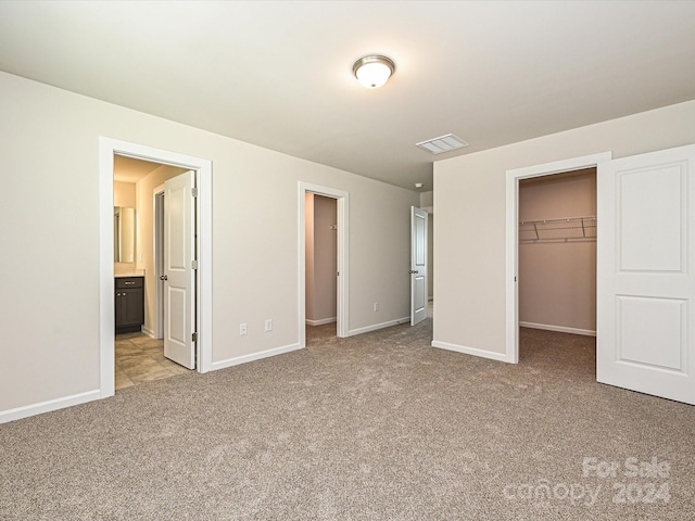 unfurnished bedroom featuring a spacious closet, light carpet, a closet, and ensuite bath