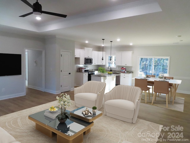 living room featuring ceiling fan, ornamental molding, a raised ceiling, and light hardwood / wood-style flooring