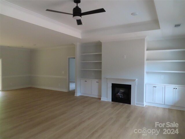 unfurnished living room featuring light wood-type flooring, ceiling fan, built in features, and a tray ceiling