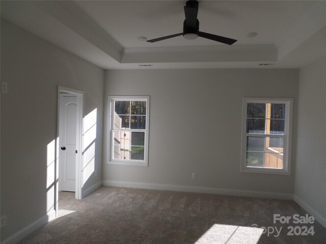 empty room with ceiling fan, crown molding, a tray ceiling, and dark carpet