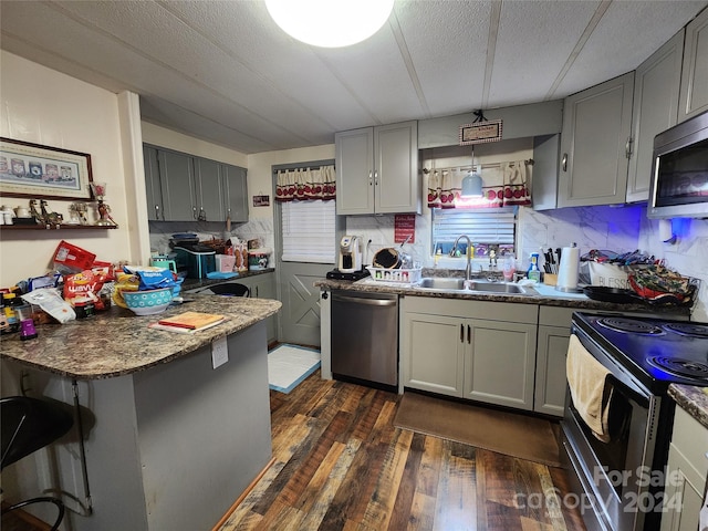 kitchen with dark wood-type flooring, backsplash, kitchen peninsula, appliances with stainless steel finishes, and sink