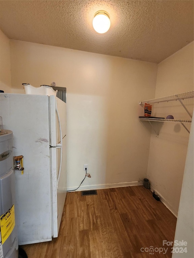 laundry area with a textured ceiling, water heater, and hardwood / wood-style flooring